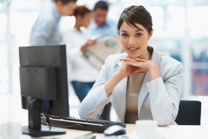 Pretty Caucasian business woman at office desk with colleagues in the back